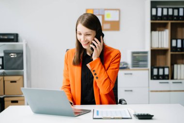 Kendine güveni tam bir iş kadını, yaratıcı ofiste masa başında otururken akıllı telefonuyla konuşuyor.
