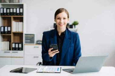 Ofisteki masada dizüstü bilgisayar ve akıllı telefon kullanan bir iş kadını.