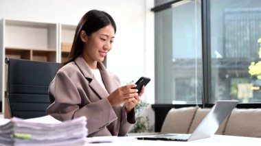 Bilgisayarda çalışan kendine güvenen bir iş kadını ve modern ofisindeki iş yerinde akıllı telefon..
