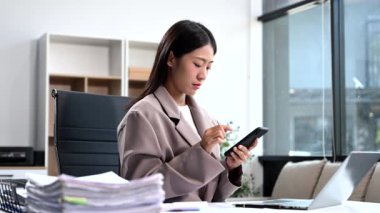 Bilgisayarda çalışan kendine güvenen bir iş kadını ve modern ofisindeki iş yerinde akıllı telefon..