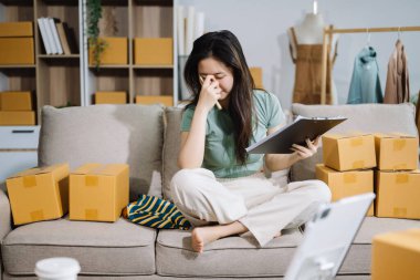 Genç Asyalı kadın, paket kutusunu hazırla ve müşteriye teslimat için panodan online siparişleri kontrol et.