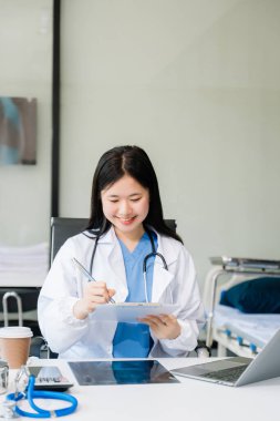 Güzel hekim doktor ofis hastanesinde kahveyle masada oturuyor. Çekici terapist, kadın pratisyen, eczacı dizüstü bilgisayar kullanıyor. 