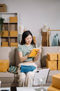 Küçük işletme girişimcisi KOBİ 'li kadın, ev ofisinde kutu, kitap ve tablet bilgisayarla çalışıyor