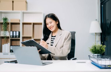 Ofisteki masada çalışan iş kadını dizüstü bilgisayar kullanıyor ve panoya yazı yazıyor. 