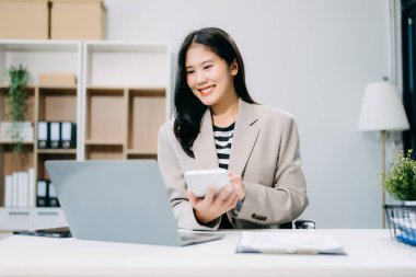 Ofisteki masada çalışan iş kadını dizüstü bilgisayar ve hesap makinesi kullanıyor.  