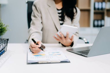 Modern ofisteki iş yerinde hesap makinesi ve laptop üzerinde çalışan kendine güvenen bir iş kadını.
