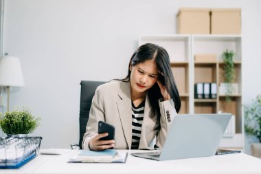 Asyalı iş kadını stresli, sıkılmış ve modern ofisteki akıllı telefondan çok fazla düşünüyor.
