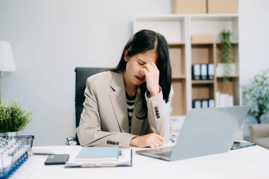 Asyalı iş kadını stresli, sıkılmış ve modern ofiste dizüstü bilgisayarla çalışmaktan çok fazla düşünüyor.