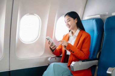 Genç Asyalı yönetici uçakta akıllı telefon kullanarak birinci sınıfta uçuyor. 