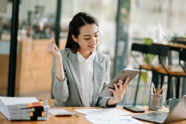 Modern ofiste dijital tablet ve dizüstü bilgisayarla finansmanı analiz eden başarılı Asyalı iş kadını 