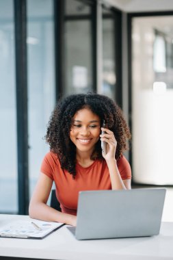Başarılı Afrikalı Amerikalı İş Kadını Laptop 'ta Finansman Analizi ve Modern Ofis' te akıllı telefondan konuşma 