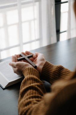 Oturan ve kutsal kitabı okuyan kadın. Ellerindeki tahta haç. Hıristiyan eğitimi kutsal yazıtların açılıp Tanrı 'ya dua etmesini sağlar.