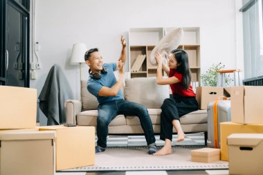 Karton kutularla mutlu Asyalı genç çift yeni bir eve taşınıyor ve yastıklarla kavga ediyor. 