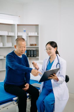 Beyaz takım elbiseli Asyalı doktor, hastanede ya da klinikte salin solüsyonu alan Asyalı yaşlıları ve yatakta yatan hastaları tartışırken not alıyor.