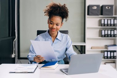 Başarılı Afrikalı Amerikalı İş Kadını Modern Ofis 'teki belge ve dizüstü bilgisayarları analiz ediyor 