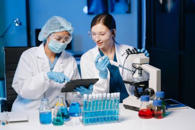 Tıp laboratuarında araştırma yapan genç bilim adamları, bir mikroskop ve tıp laboratuvarında dijital tablet kullanan araştırmacılar,.  