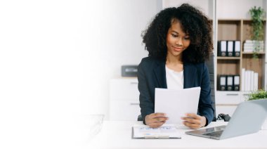 Belgelerle çalışan genç bir iş kadını ve ofiste çalışmak için dizüstü bilgisayar kullanıyor. 