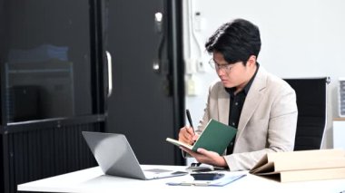 Ofisindeki masada dizüstü bilgisayar ve akıllı telefonla çalışan genç bir işadamı.