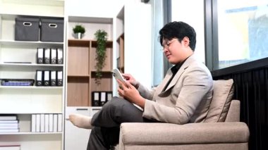 Genç Asyalı iş adamı iş yerinde akıllı telefon kullanıyor 