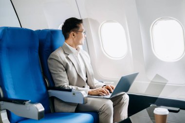 Genç Asyalı yönetici dizüstü bilgisayar, akıllı telefon ve kahveyle birinci sınıfta başarılı oldu. 