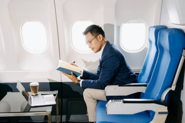 Genç Asyalı yönetici dizüstü bilgisayar, akıllı telefon, not defteri ve kahveyle birinci sınıfta başarılı.. 