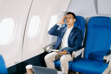 Genç Asyalı yönetici dizüstü bilgisayar, kahve ve not defteriyle birinci sınıfta başarılı oldu  