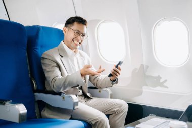 Genç Asyalı yönetici dizüstü bilgisayar, akıllı telefon ve kahveyle birinci sınıfta başarılı oldu. 