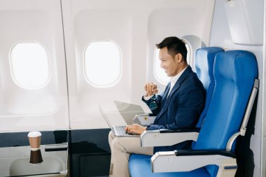 Genç Asyalı yönetici dizüstü bilgisayar, akıllı telefon ve kahveyle birinci sınıfta başarılı oldu. 