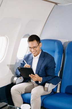 Genç Asyalı yönetici dijital tablet, telefon ve kahveyle birinci sınıfta başarılı oldu. 