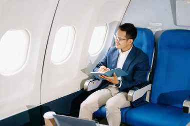 Genç Asyalı yönetici dizüstü bilgisayar, kahve ve not defteriyle birinci sınıfta başarılı oldu  