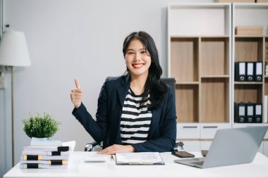 Gülümseyen iş kadını başparmak gösteriyor ve ofiste çalışmak için dizüstü bilgisayar kullanıyor. 