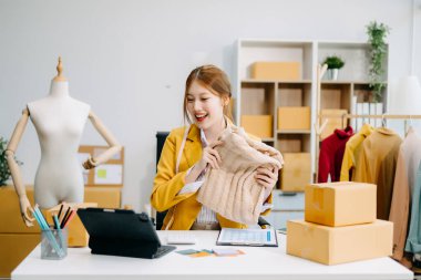 Asyalı terzi kadın terzi atölyesinde giysiler üzerinde çalışıyor. Stüdyoda dijital tablet üzerinde çalışan genç ve güzel bir iş kadını. 