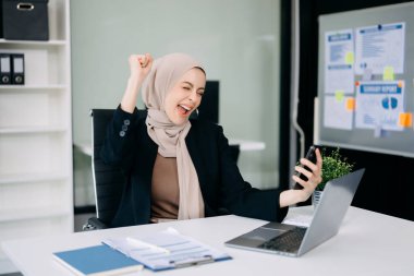 Ofiste çalışmak için akıllı telefon dizüstü bilgisayarı kullanan çekici bir iş kadını.  