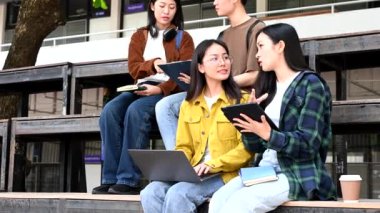 Genç Asyalı kolej öğrencileri kampüs parkında dizüstü bilgisayar, tablet bilgisayar ve kahve ile çalışıyorlar.