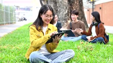 Genç Asyalı kolej öğrencileri grubu kampüs parkında tablet bilgisayarla çalışıyor.