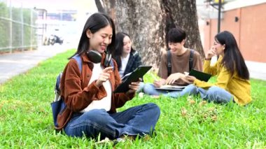 Genç Asyalı kolej öğrencileri grubu kampüs parkında tablet bilgisayarla çalışıyor.