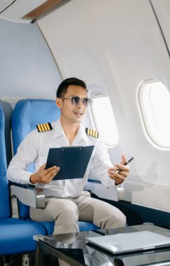 Asyalı kendinden emin üniformalı erkek pilot yolcu koltuğunda oturuyor ve çalışıyor. 