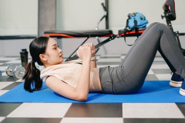 Azimli Asyalı kadın spor salonunda kilo veriyor ve minder üzerinde karın kasları egzersizi yapıyor. Spor ve eğlence konsepti. Spor giyim sektöründe güzel bir kadın 