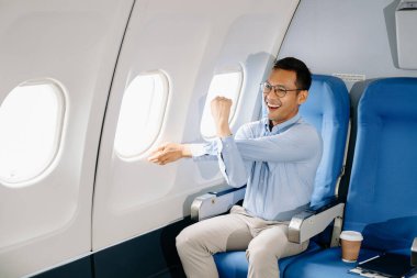 Uçakta bir koltukta oturan genç Asyalı, seyahate çıkmaktan mutlu.. 