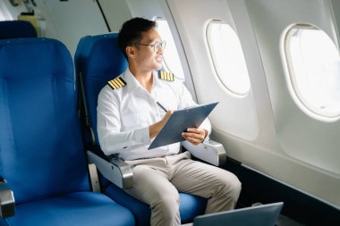 Asyalı kendinden emin üniformalı erkek pilot yolcu koltuğunda oturuyor ve çalışıyor. 