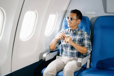 Uçakta bir koltukta oturan Asyalı adam, pencereden dışarı bakıyor ve kahve içiyor, seyahate çıkıyor.. 