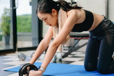 Spor salonundaki kararlı Asyalı kadın kas tekeriyle egzersiz yapıyor. Spor ve eğlence konsepti. Spor giyim sektöründe güzel bir kadın 