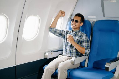 Mutlu Asyalı adam uçakta bir koltukta oturuyor ve kahve içiyor, seyahate çıkıyor.. 