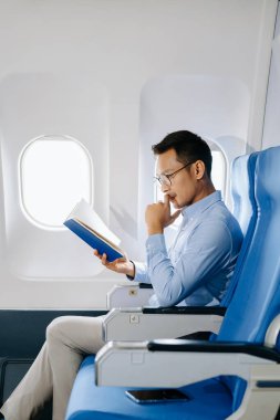 Ciddi bir Asyalı adam uçakta oturmuş kitap okuyor, tatile çıkıyor.. 