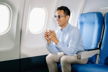 Çekici Asyalı erkek uçak yolcusu rahat koltukta oturup kahve içiyor.. 