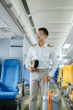 Üniformalı Asyalı gülümseyen erkek pilot uçağın içinde duruyor.