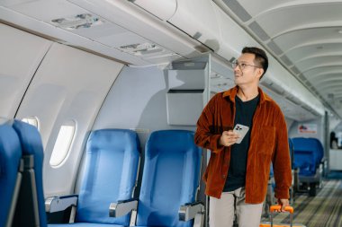 Bavullu Asyalı bir adam uçakta yer arıyor, seyahate çıkıyor.