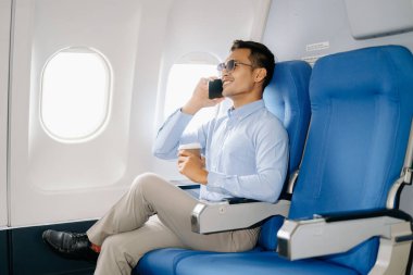 Akıllı telefonda konuşurken rahat koltukta oturan Asyalı erkek yolcu. Seyahat, tatil konsepti 