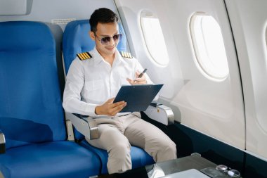 Asyalı kendinden emin üniformalı erkek pilot yolcu koltuğunda oturuyor ve çalışıyor. 