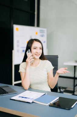 Genç ve güzel Asyalı iş kadını iş yerinde telefonla konuşuyor.. 